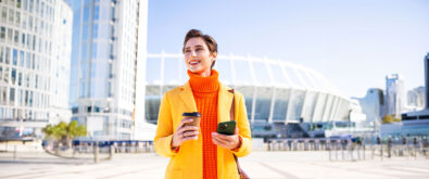 Woman holding a cup of coffee and performing a transaction on her smartphone