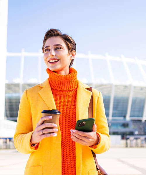 Woman holding a cup of coffee and performing a transaction on her smartphone