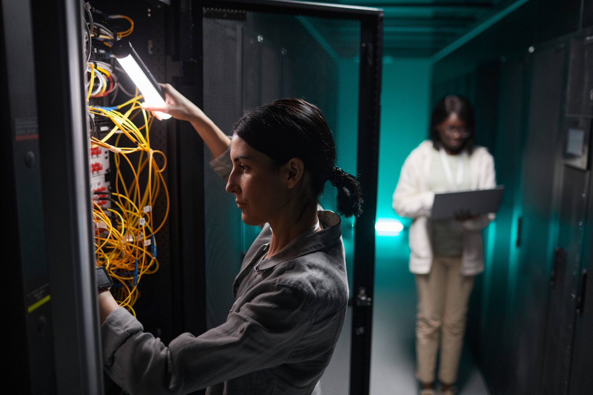 Women managing server room by pluging cables and setting up the system